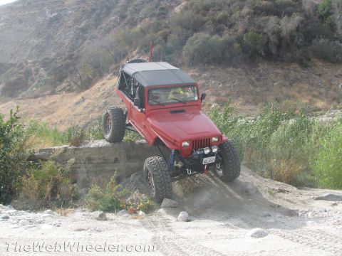 1987 Suzuki Samurai - A red off-road vehicle navigates a challenging dirt path with steep inclines.
