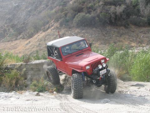 1987 Suzuki Samurai - A red Jeep Wrangler navigates a rocky trail, its lifted suspension and off-road modifications.