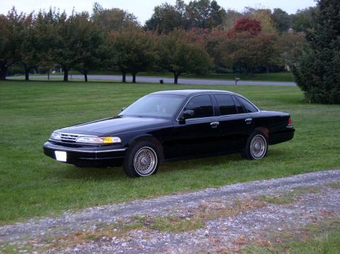 1997 Ford Crown Victoria - A black 1997 Ford Crown Victoria sedan is parked on a grassy lawn with trees in the background.