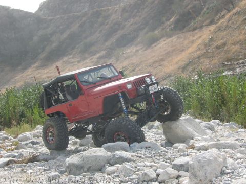 1987 Suzuki Samurai - A red Jeep navigates a rocky terrain with its suspension articulated.