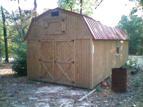 1992 Ford F-150 - Wooden gambrel-roof storage shed with a red metal roof, double barn-style doors with X bracing and a loft hatch, sitting on bare dirt in a…