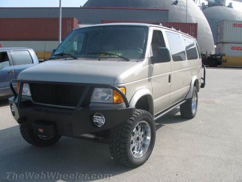 1990 Ford Bronco - tan lifted Ford Econoline van fitted with a heavy steel front bumper, brush guard, winch and chunky off-road tires.
