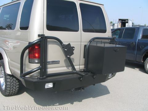 1990 Ford Bronco - Rear view of a tan Ford E350 van fitted with a heavy steel bumper carrying a swing-out tire mount and black storage box.