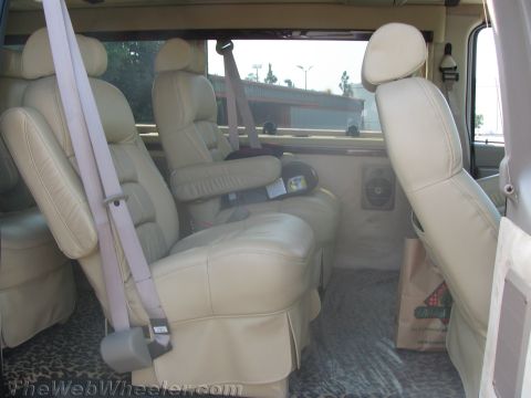 1990 Ford Bronco - Interior of a conversion van showing tan leather captain's chairs and a folded bench seat over leopard-print floor mats.