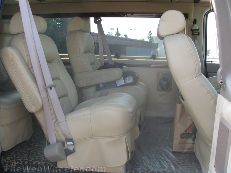 Tan leather captain's chairs and bench inside a conversion van's rear interior