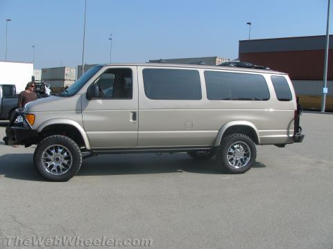 1990 Ford Bronco - Side profile of a tan lifted Ford Econoline van on chrome wheels and off-road tires with a steel front bumper, in a paved lot.