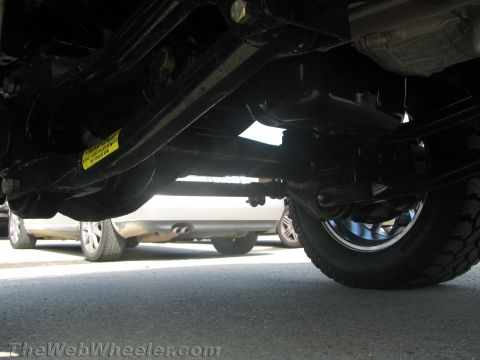 1990 Ford Bronco - Low underside view of a lifted van showing the frame, rear axle, driveshaft and suspension components above the pavement.