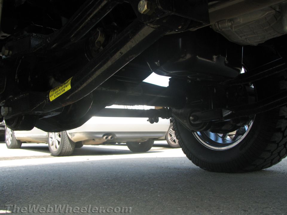 Underside view of a lifted van's chassis, axle and suspension over pavement