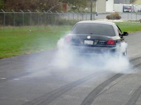 1997 Ford Crown Victoria - A black sedan is performing a burnout, creating a large cloud of smoke.