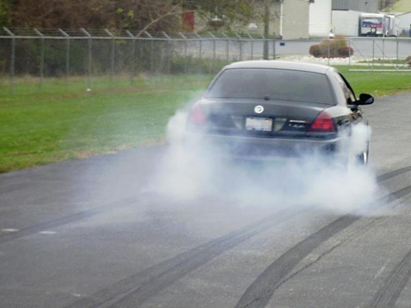Black sedan doing a burnout, kicking up a lot of smoke