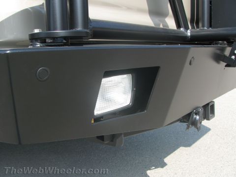 1990 Ford Bronco - Close-up of a van's black steel bumper corner showing a rectangular driving light, tube uprights and a hitch receiver.