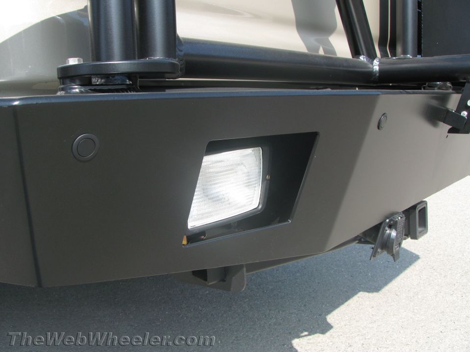 Close-up of a black steel bumper corner with a rectangular driving light and hitch receiver