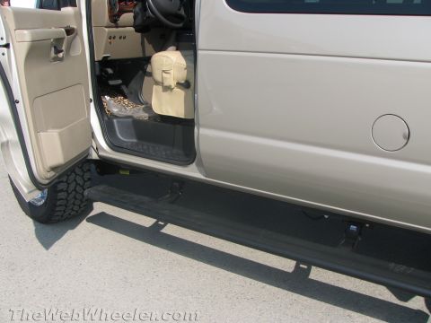 1990 Ford Bronco - Open passenger-side door of a tan Ford van revealing the tan interior, off-road tire, side running board and fuel filler cap.