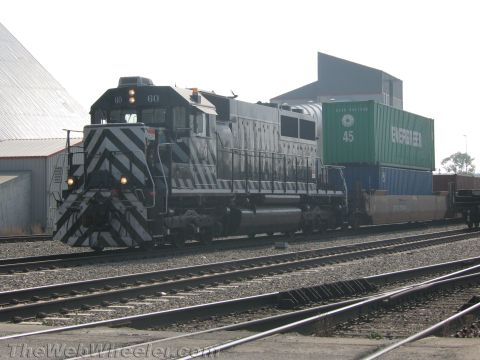 1990 Ford Bronco - dark green diesel locomotive numbered 60 pulls a green Evergreen shipping container across multiple tracks in a rail yard.