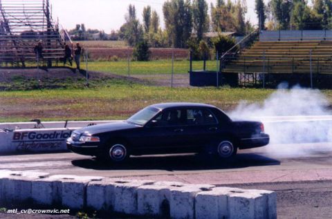 1997 Ford Crown Victoria - A dark 1997 Ford Crown Victoria sedan performs a burnout on a drag strip, with smoke billowing from its tires.