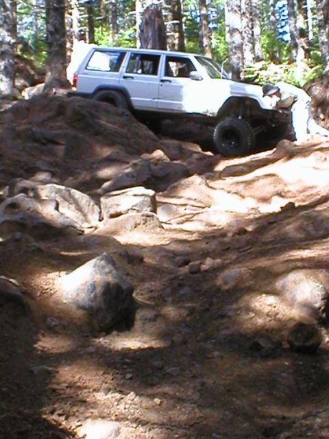 2005 Jeep Wrangler - A white Jeep Cherokee XJ navigates a challenging rocky trail in a wooded area.
