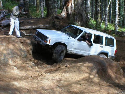 2005 Jeep Wrangler - A white Jeep Cherokee XJ navigates a challenging off-road trail in a wooded area.