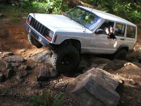 2005 Jeep Wrangler - A white Jeep Cherokee XJ navigates a rocky trail with its tires angled on large boulders.