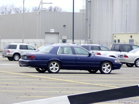 1997 Ford Crown Victoria - A blue 1997 Ford Crown Victoria sedan is parked in a lot with other vehicles.