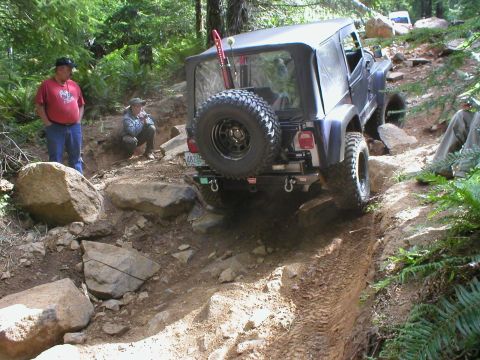 2005 Jeep Wrangler - A dark Jeep Wrangler navigates a challenging rocky trail, with another vehicle visible in the background.