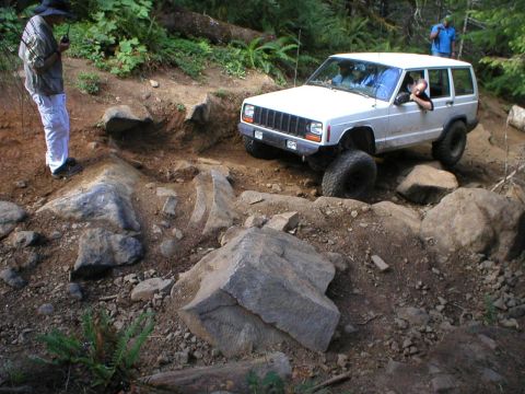 2005 Jeep Wrangler - A white Jeep Cherokee XJ tackles a challenging rocky off-road course, demonstrating its capability on uneven terrain.