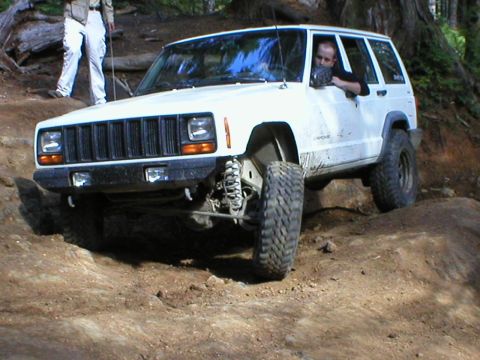 2005 Jeep Wrangler - A white Jeep Cherokee XJ navigates a challenging off-road trail with a driver visible through the window.