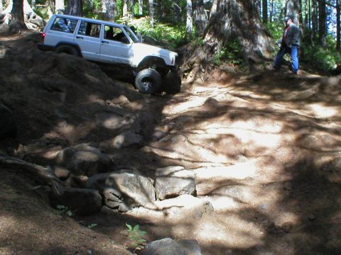 2005 Jeep Wrangler - A white Jeep Cherokee XJ navigates a challenging off-road trail with a person watching in the background.