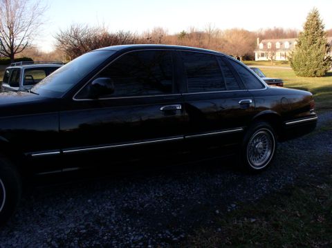 1997 Ford Crown Victoria - A black 1997 Ford Crown Victoria is parked in a gravel driveway with a house and trees in the background.