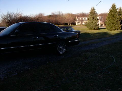 1997 Ford Crown Victoria - A black 1997 Ford Crown Victoria sedan is parked in a grassy area with a house in the background.