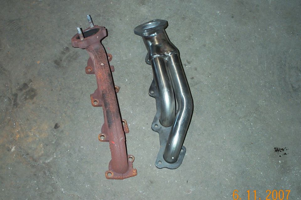 Rusty cast-iron exhaust manifold next to new stainless shorty header on concrete floor
