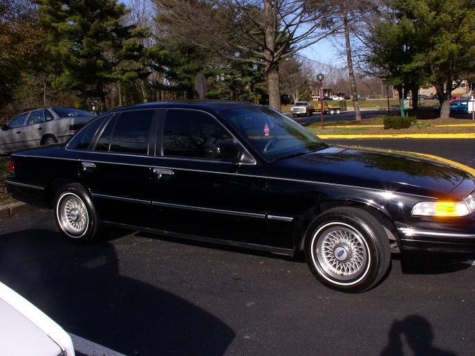 Black 1997 Ford Crown Victoria parked on asphalt, side view. Another car is visible behind it