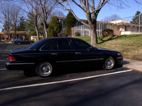 1997 Ford Crown Victoria - A black 1997 Ford Crown Victoria sedan is parked in a lot with another car visible in the background.