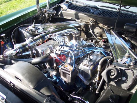 1973 Ford Mustang - The engine bay of a green 1973 Ford Mustang shows a V8 engine with chrome valve covers and intake manifold.