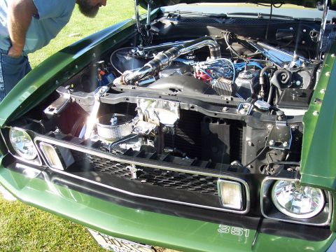 1973 Ford Mustang - A man inspects the engine bay of a green 1970s Ford Mustang, chrome accents and custom piping.