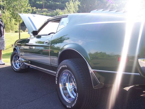 1973 Ford Mustang - A green muscle car is parked outside with its hood up, showing off its chrome wheels and tires.