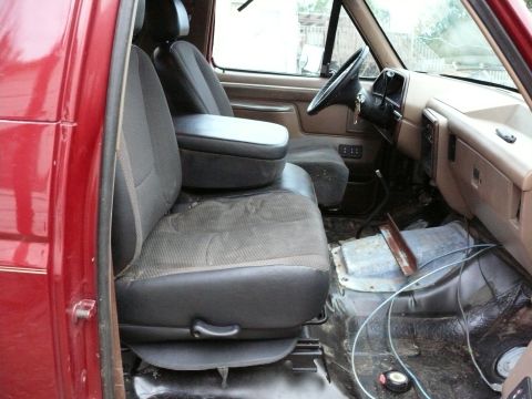 1988 Ford Bronco - The interior of a red truck, focusing on the seats and dashboard area. The floor appears to be in a state of disrepair.