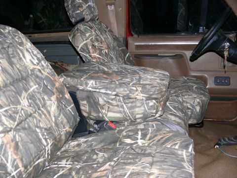 1988 Ford Bronco - The interior of a vehicle is shown, camouflage seat covers over the front seats and a glimpse of the dashboard and steering wheel.