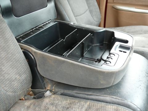 1988 Ford Bronco - The interior of a vehicle shows a gray fabric center console with a black plastic storage compartment and lid.
