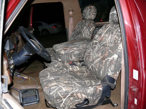 1988 Ford Bronco - The interior of a vehicle shows camouflage seat covers and a steering wheel, with another car visible outside.