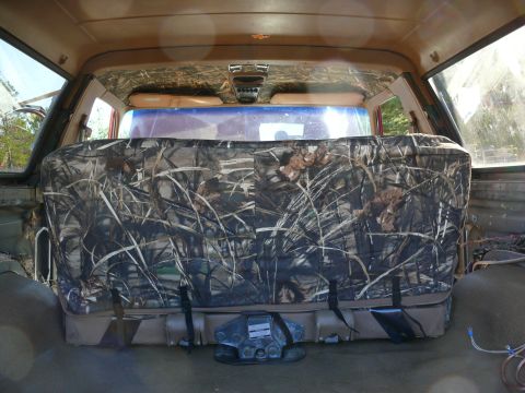 1988 Ford Bronco - The rear interior of a vehicle features a camouflage seat cover over the rear bench seat, with a SuperMotors logo visible at the bottom rig…