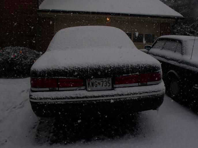 Rear of a 1997 Ford Crown Victoria covered in snow, license plate KW6 735. Another car is parked to the right