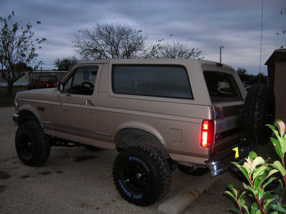 Lifted tan Ford SUV with hardtop and rear swing-out spare on black wheels and mud tires at dusk