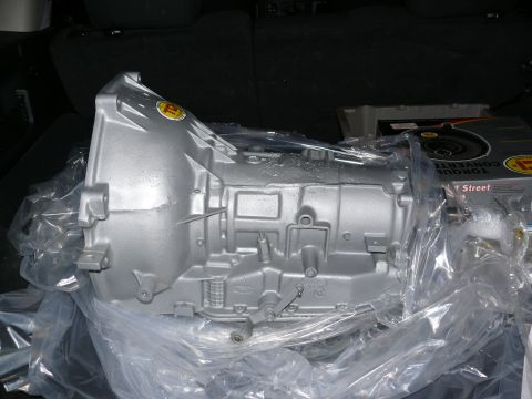 1988 Ford Bronco - A silver transmission part is shown in plastic wrap, with a box labeled 'TORQUE CONVERTER' visible behind it.