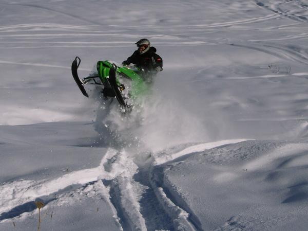 Green snowmobile jumping through deep powder snow with rider in helmet