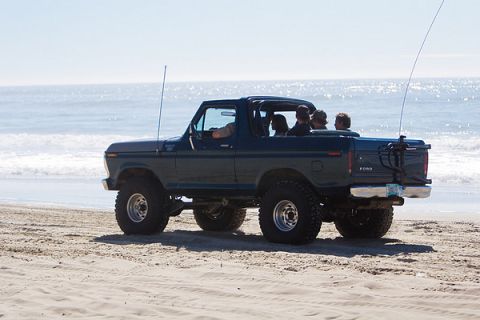 1979 Ford Bronco - Ford Bronco with passengers drives along the beach on a sunny day.