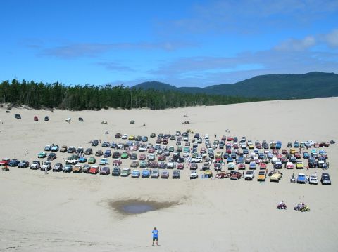 1979 Ford Bronco - A large gathering of off-road vehicles parked on a sandy landscape under a blue sky.