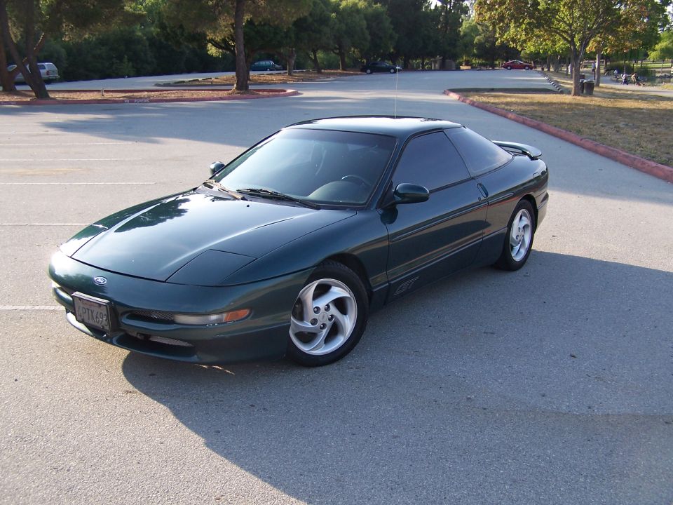 Dark green Ford Probe GT hatchback parked in an empty tree-lined parking lot