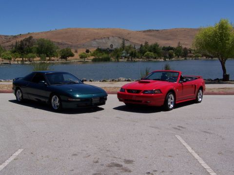 1996 Ford Probe - A green Ford Probe and a red Ford Mustang convertible are parked side-by-side in front of a lake.
