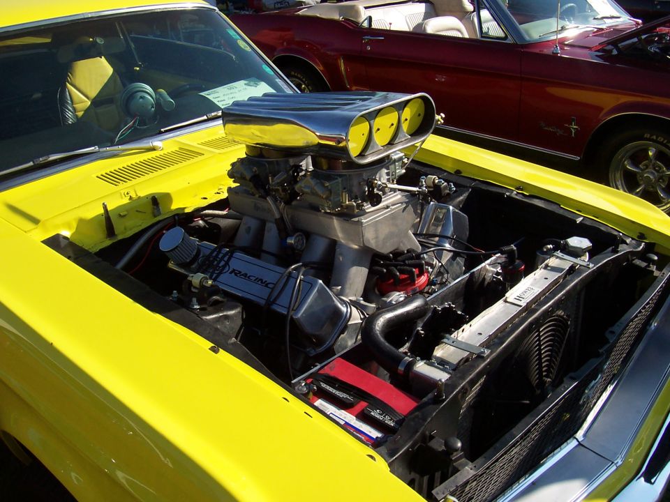 Yellow 1973 Ford Mustang engine with chrome scoop and dual carburetors