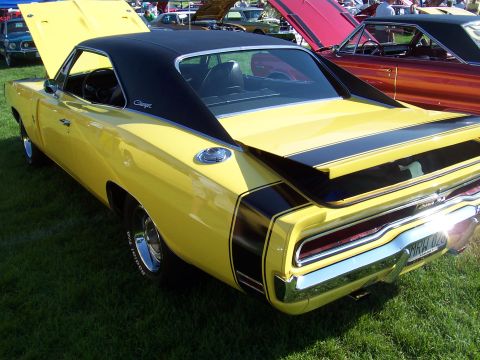 1973 Ford Mustang - A yellow 1970 Dodge Charger with black racing stripes and a black vinyl roof is displayed on a grassy field with other vehicles.